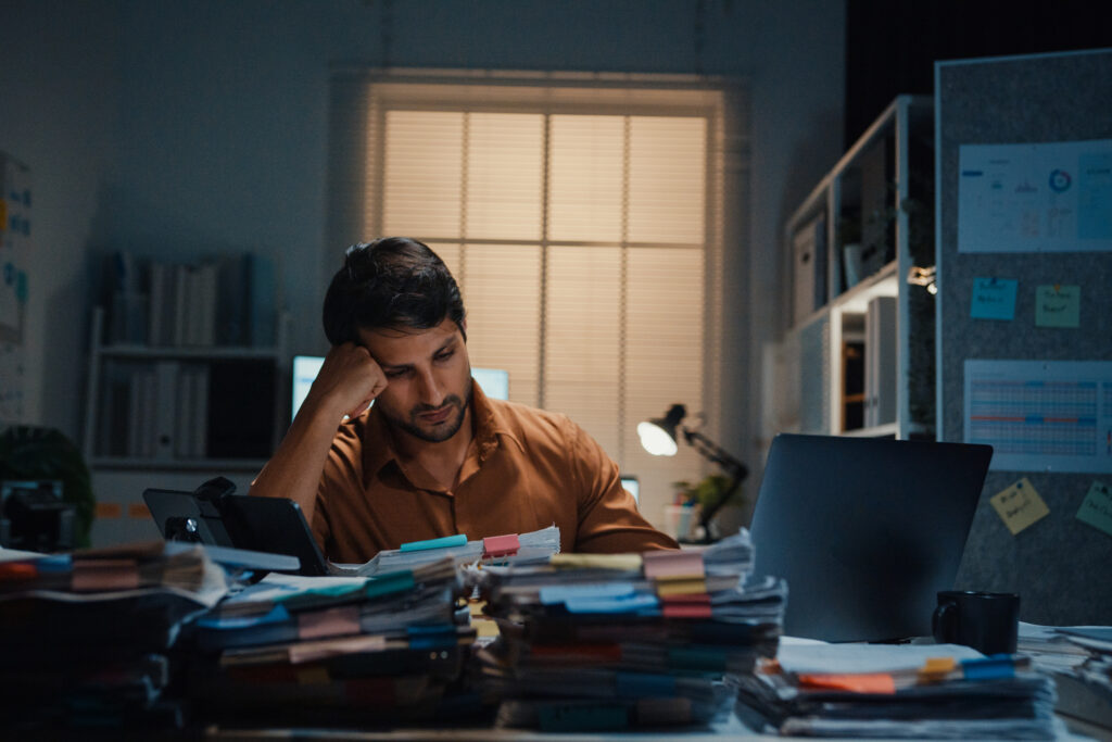 Stressed out young Latino businessman sits a desk piled high with files